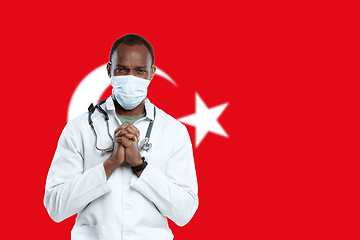 Image showing Young doctor with stethoscope and face mask praying for God with Turkey national flag on background