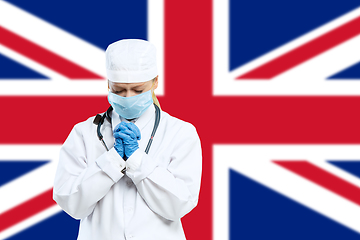 Image showing Female young doctor with stethoscope and face mask praying for God with United Kingdom national flag on background