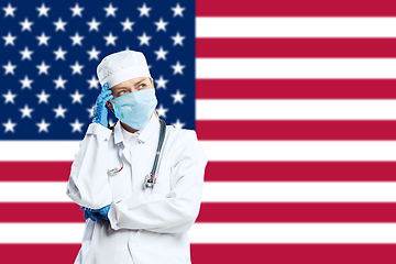 Image showing Female young doctor with stethoscope and face mask praying for God with USA national flag on background