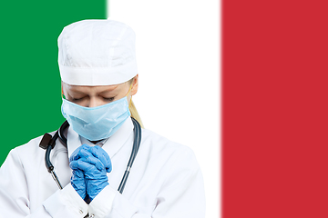 Image showing Female young doctor with stethoscope and face mask praying for God with Italy national flag on background