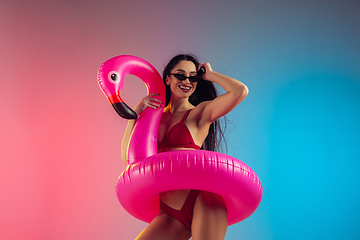 Image showing Fashion portrait of young fit and sportive woman with rubber flamingo in stylish red swimwear on gradient background. Perfect body ready for summertime.