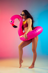 Image showing Fashion portrait of young fit and sportive woman with rubber flamingo in stylish red swimwear on gradient background. Perfect body ready for summertime.