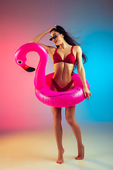 Image showing Fashion portrait of young fit and sportive woman with rubber flamingo in stylish red swimwear on gradient background. Perfect body ready for summertime.