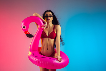 Image showing Fashion portrait of young fit and sportive woman with rubber flamingo in stylish red swimwear on gradient background. Perfect body ready for summertime.