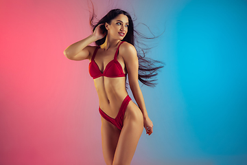 Image showing Fashion portrait of young fit and sportive woman in stylish red luxury swimwear on gradient background. Perfect body ready for summertime.