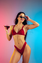 Image showing Fashion portrait of young fit and sportive woman with cocktail in stylish red luxury swimwear on gradient background. Perfect body ready for summertime.