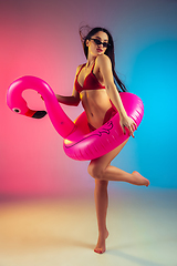 Image showing Fashion portrait of young fit and sportive woman with rubber flamingo in stylish red swimwear on gradient background. Perfect body ready for summertime.