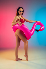 Image showing Fashion portrait of young fit and sportive woman with rubber flamingo in stylish red swimwear on gradient background. Perfect body ready for summertime.