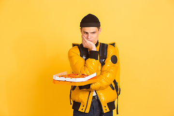 Image showing Contacless delivery service during quarantine. Man delivers food and shopping bags during insulation. Emotions of deliveryman isolated on yellow background.