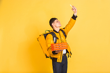 Image showing Contacless delivery service during quarantine. Man delivers food and shopping bags during insulation. Emotions of deliveryman isolated on yellow background.