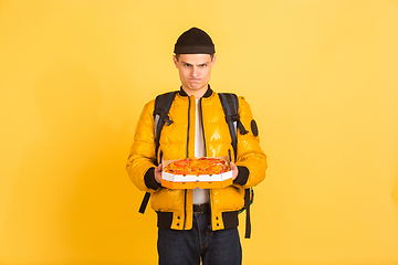 Image showing Contacless delivery service during quarantine. Man delivers food and shopping bags during insulation. Emotions of deliveryman isolated on yellow background.