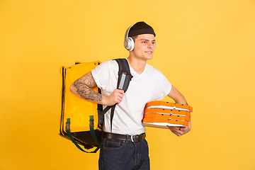 Image showing Contacless delivery service during quarantine. Man delivers food and shopping bags during insulation. Emotions of deliveryman isolated on yellow background.