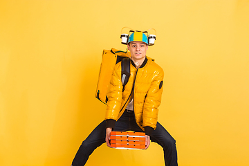 Image showing Contacless delivery service during quarantine. Man delivers food and shopping bags during insulation. Emotions of deliveryman isolated on yellow background.