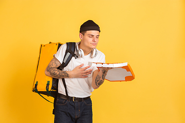 Image showing Contacless delivery service during quarantine. Man delivers food and shopping bags during insulation. Emotions of deliveryman isolated on yellow background.