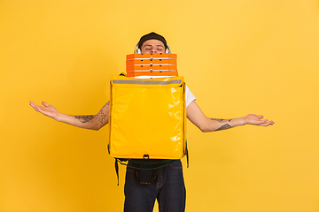 Image showing Contacless delivery service during quarantine. Man delivers food and shopping bags during insulation. Emotions of deliveryman isolated on yellow background.