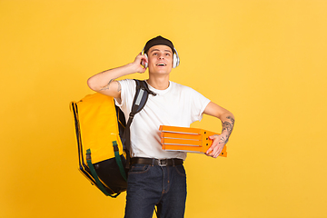 Image showing Contacless delivery service during quarantine. Man delivers food and shopping bags during insulation. Emotions of deliveryman isolated on yellow background.