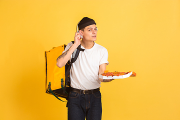 Image showing Contacless delivery service during quarantine. Man delivers food and shopping bags during insulation. Emotions of deliveryman isolated on yellow background.