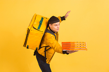 Image showing Contacless delivery service during quarantine. Man delivers food and shopping bags during insulation. Emotions of deliveryman isolated on yellow background.