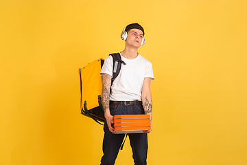 Image showing Contacless delivery service during quarantine. Man delivers food and shopping bags during insulation. Emotions of deliveryman isolated on yellow background.