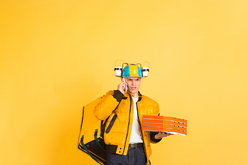 Image showing Contacless delivery service during quarantine. Man delivers food and shopping bags during insulation. Emotions of deliveryman isolated on yellow background.