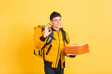 Image showing Contacless delivery service during quarantine. Man delivers food and shopping bags during insulation. Emotions of deliveryman isolated on yellow background.