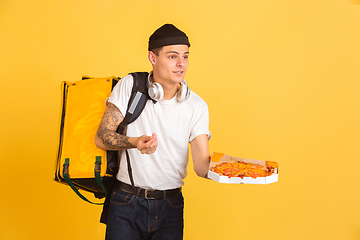 Image showing Contacless delivery service during quarantine. Man delivers food and shopping bags during insulation. Emotions of deliveryman isolated on yellow background.