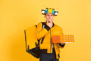 Image showing Contacless delivery service during quarantine. Man delivers food and shopping bags during insulation. Emotions of deliveryman isolated on yellow background.