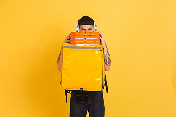 Image showing Contacless delivery service during quarantine. Man delivers food and shopping bags during insulation. Emotions of deliveryman isolated on yellow background.