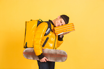 Image showing Contacless delivery service during quarantine. Man delivers food and shopping bags during insulation. Emotions of deliveryman isolated on yellow background.