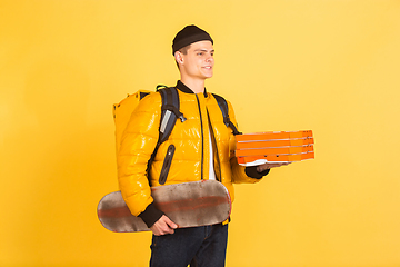 Image showing Contacless delivery service during quarantine. Man delivers food and shopping bags during insulation. Emotions of deliveryman isolated on yellow background.