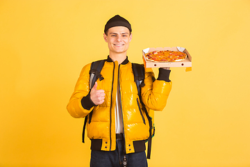 Image showing Contacless delivery service during quarantine. Man delivers food and shopping bags during insulation. Emotions of deliveryman isolated on yellow background.