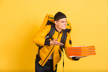 Image showing Contacless delivery service during quarantine. Man delivers food and shopping bags during insulation. Emotions of deliveryman isolated on yellow background.