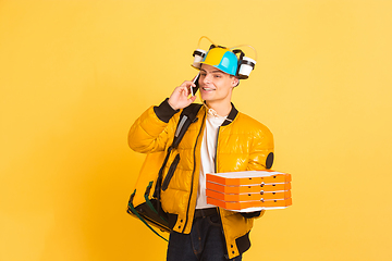 Image showing Contacless delivery service during quarantine. Man delivers food and shopping bags during insulation. Emotions of deliveryman isolated on yellow background.