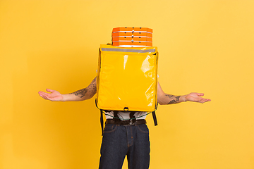 Image showing Contacless delivery service during quarantine. Man delivers food and shopping bags during insulation. Emotions of deliveryman isolated on yellow background.