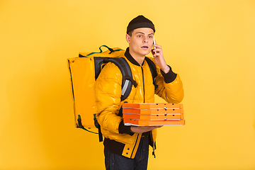 Image showing Contacless delivery service during quarantine. Man delivers food and shopping bags during insulation. Emotions of deliveryman isolated on yellow background.