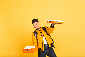 Image showing Contacless delivery service during quarantine. Man delivers food and shopping bags during insulation. Emotions of deliveryman isolated on yellow background.