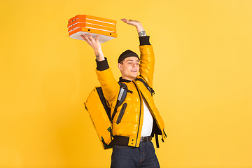 Image showing Contacless delivery service during quarantine. Man delivers food and shopping bags during insulation. Emotions of deliveryman isolated on yellow background.