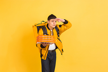 Image showing Contacless delivery service during quarantine. Man delivers food and shopping bags during insulation. Emotions of deliveryman isolated on yellow background.