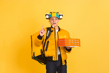 Image showing Contacless delivery service during quarantine. Man delivers food and shopping bags during insulation. Emotions of deliveryman isolated on yellow background.