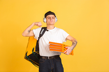 Image showing Contacless delivery service during quarantine. Man delivers food and shopping bags during insulation. Emotions of deliveryman isolated on yellow background.