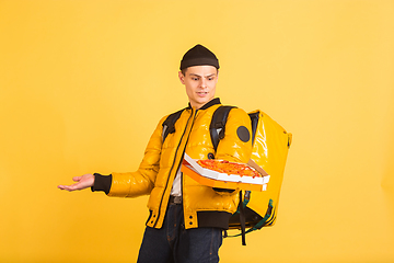 Image showing Contacless delivery service during quarantine. Man delivers food and shopping bags during insulation. Emotions of deliveryman isolated on yellow background.