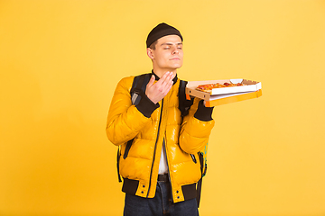 Image showing Contacless delivery service during quarantine. Man delivers food and shopping bags during insulation. Emotions of deliveryman isolated on yellow background.