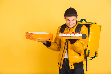 Image showing Contacless delivery service during quarantine. Man delivers food and shopping bags during insulation. Emotions of deliveryman isolated on yellow background.