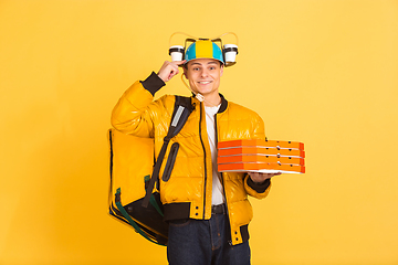 Image showing Contacless delivery service during quarantine. Man delivers food and shopping bags during insulation. Emotions of deliveryman isolated on yellow background.