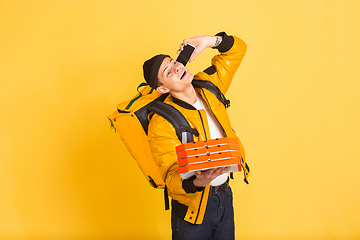 Image showing Contacless delivery service during quarantine. Man delivers food and shopping bags during insulation. Emotions of deliveryman isolated on yellow background.