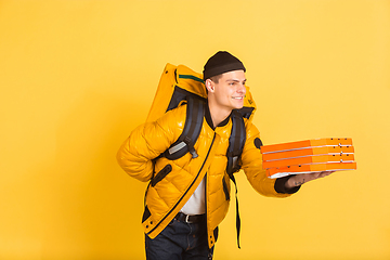 Image showing Contacless delivery service during quarantine. Man delivers food and shopping bags during insulation. Emotions of deliveryman isolated on yellow background.