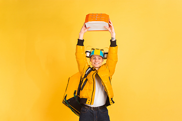 Image showing Contacless delivery service during quarantine. Man delivers food and shopping bags during insulation. Emotions of deliveryman isolated on yellow background.