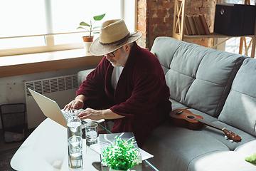 Image showing Mature senior older man during quarantine, realizing how important stay at home during virus outbreak, giving concert of taking online lessons of guitar playing