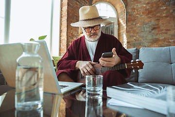 Image showing Mature senior older man during quarantine, realizing how important stay at home during virus outbreak, giving concert of taking online lessons of guitar playing