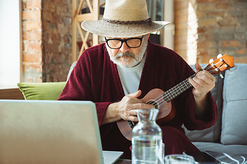 Image showing Mature senior older man during quarantine, realizing how important stay at home during virus outbreak, giving concert of taking online lessons of guitar playing